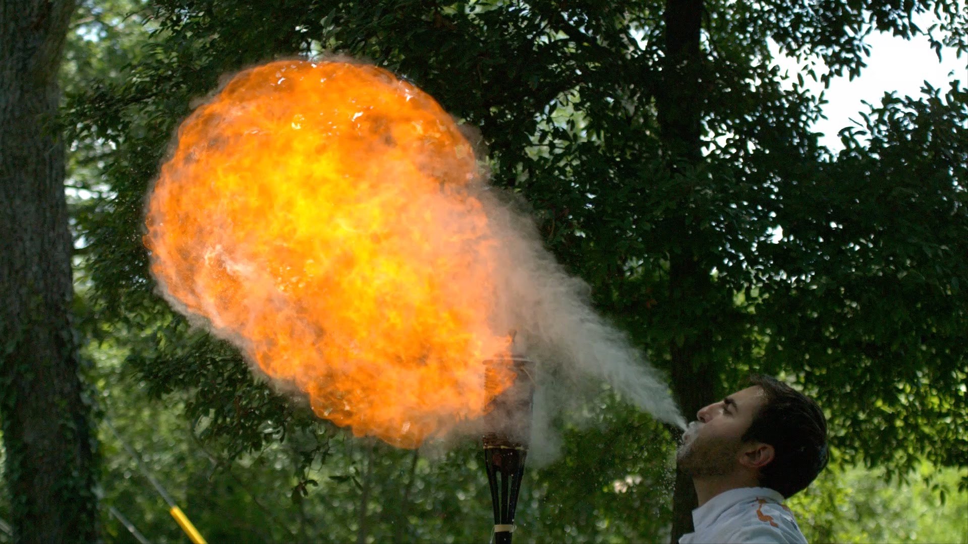 Super Slow-Motion Video of a Man Breathing Fire by Blowing Corn Starch Over  a Lit Tiki Torch