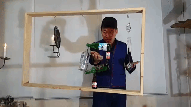 Balancing Expert Stacks 5 Bottles on One Another Inside of a Wobbly Wooden Frame