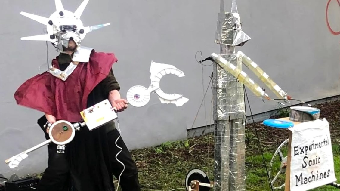 Masked Musician Plays Fantastical Handmade Instruments Alongside a Robotic Drummer Named Ernie